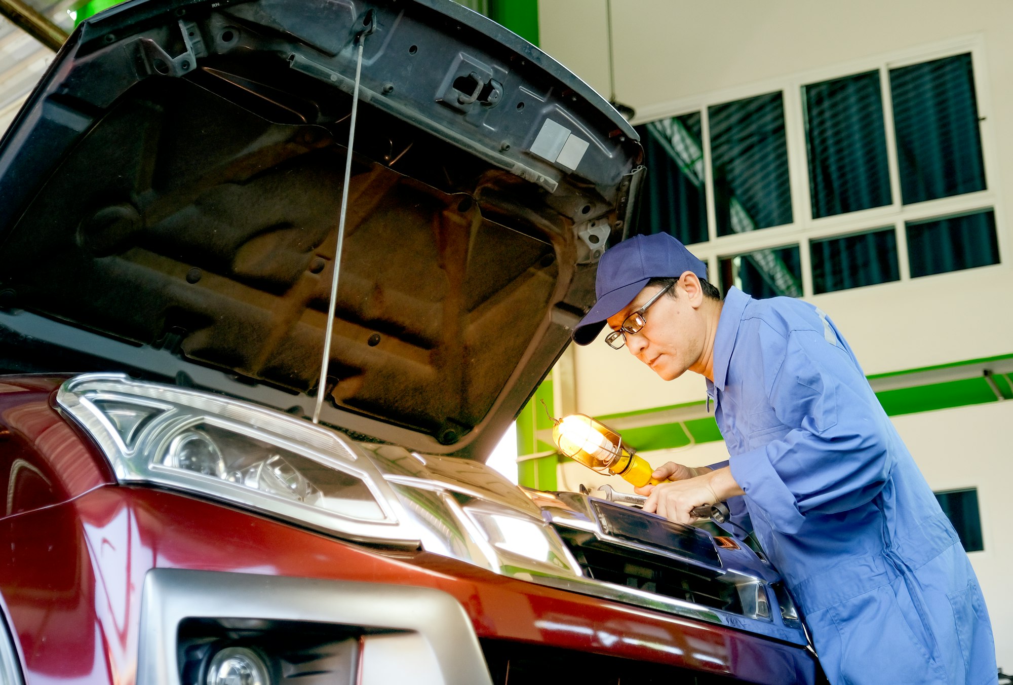 Asian automotive mechanic with blue uniform use lamp and wrench to fix the problem