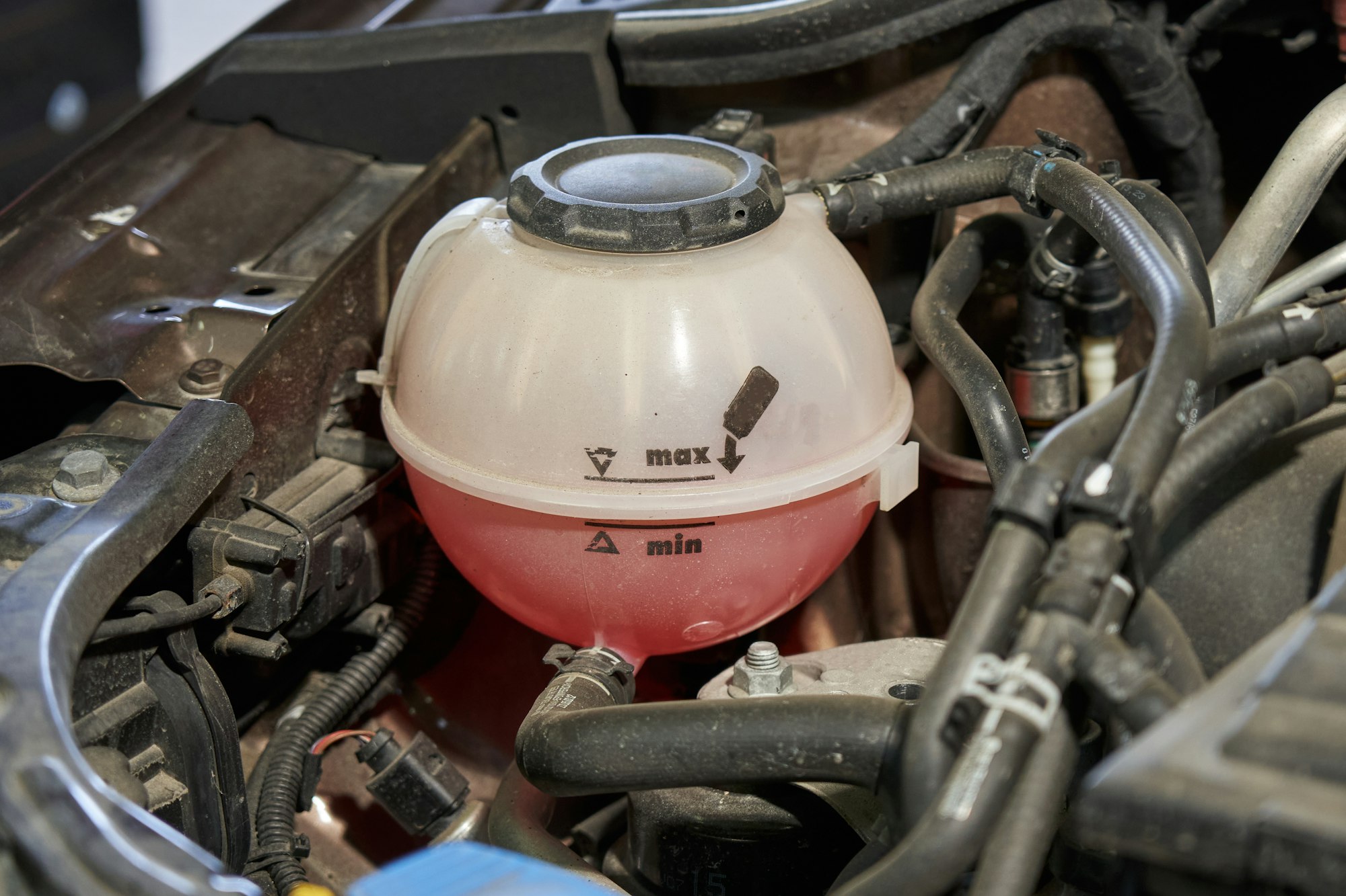 expansion tank of the car cooling system with pink antifreeze and black tubes of the engine